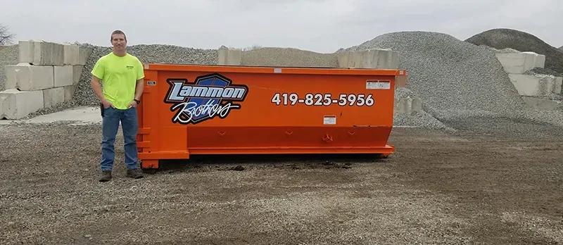 Owner standing beside a 10-yard Lammon Brothers roll-off dumpster for scale