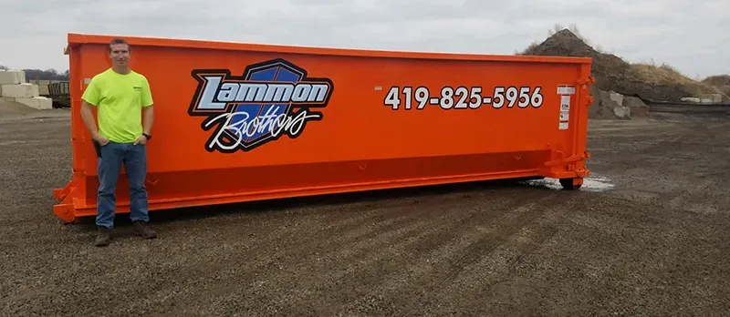 Owner standing beside a 30-yard Lammon Brothers roll-off dumpster for scale